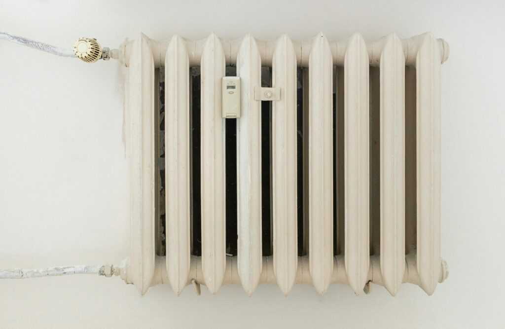 A classic white metal radiator on a plain wall, showcasing minimalist interior design.